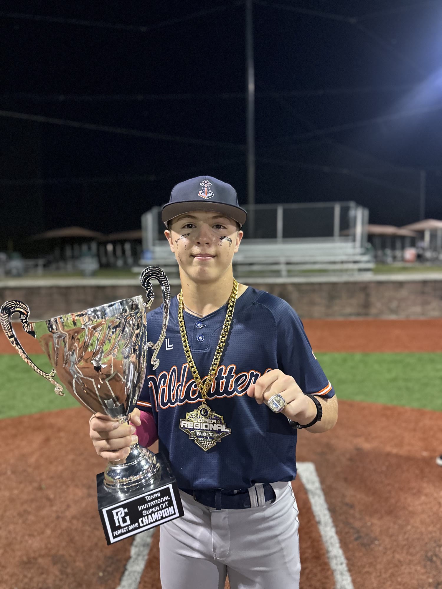 Brayden Palomino holding the Perfect Game Texas Invitational Super NIT championship trophy, chain, and ring